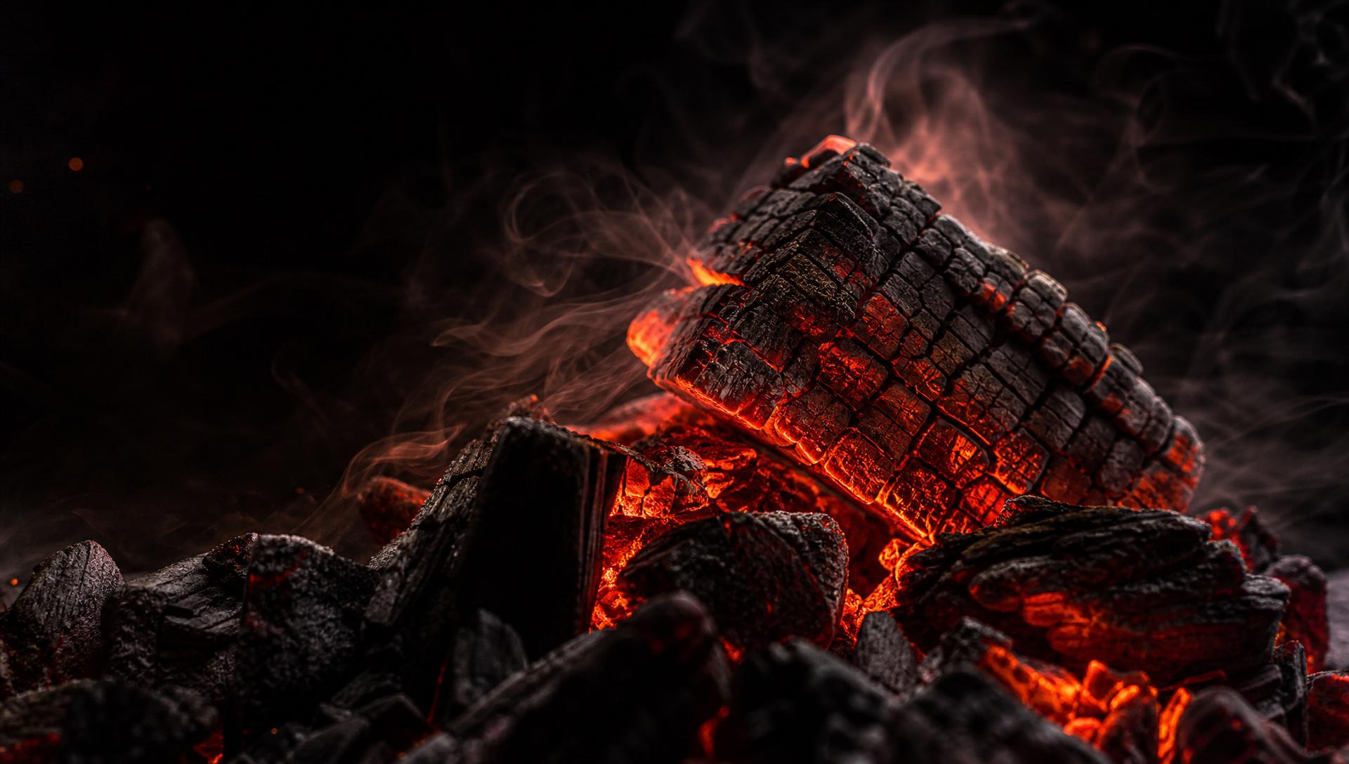 Macro of glowing red-hot FLAMORA charcoal embers in dark atmosphere